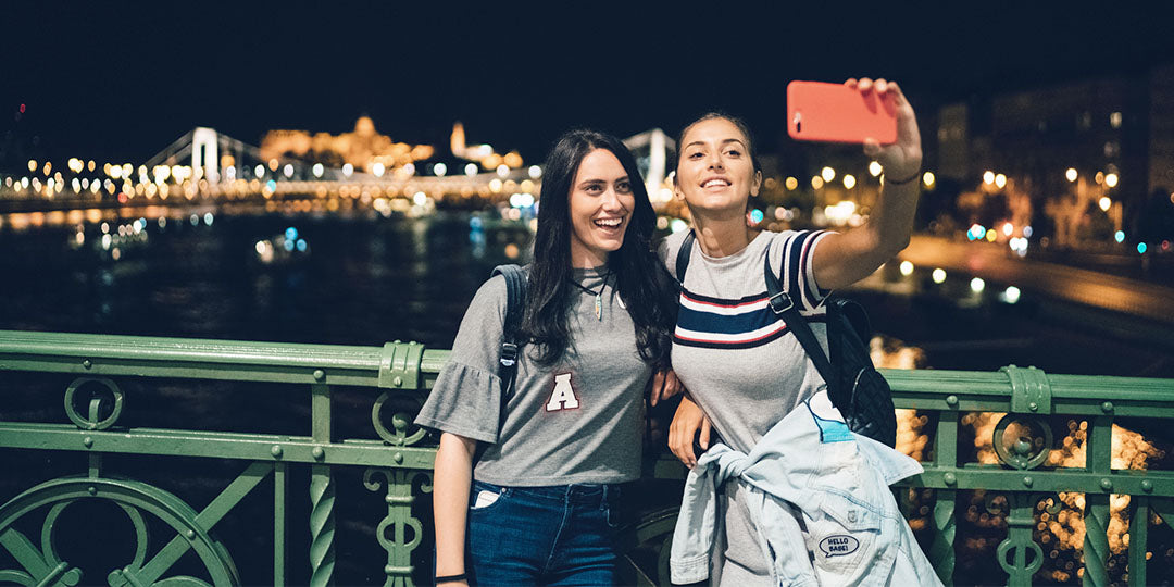 Two friends are gathered in the evening taking photos in front of a bridge with lots of lights.